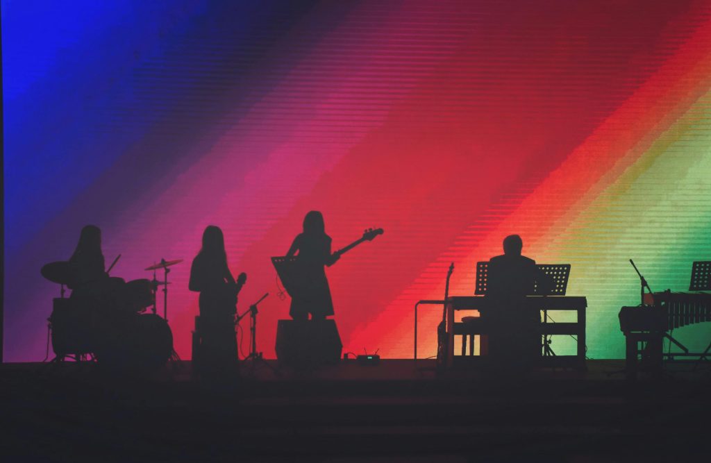 Silhouette of musicians performing on stage with vibrant colorful lighting.