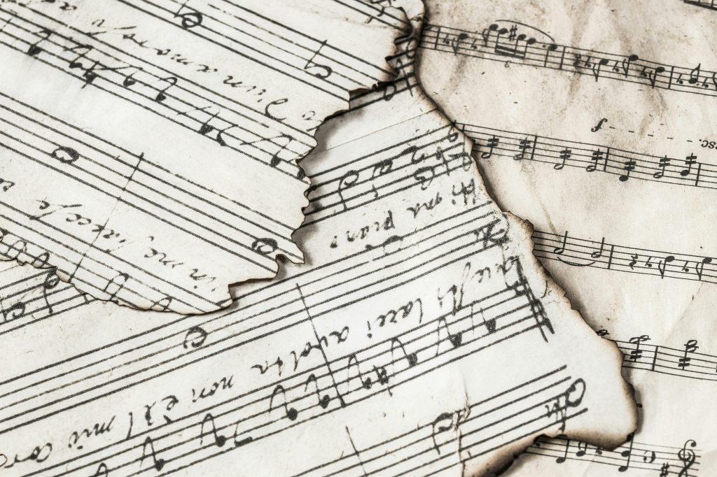Close-up of aged, burnt music sheets displaying musical notes and compositions in detail.